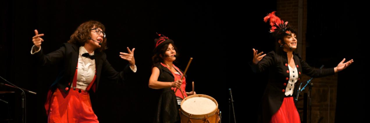 Fotografía de la compañía en escena, disfrazada de maestras de ceremonia tocando y cantando 