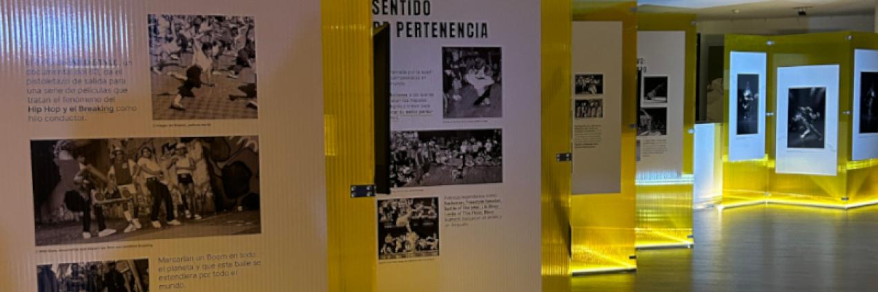 Fotografía de la sala de exposición con unos metacrilatos amarillos con fotografías en blanco y negro