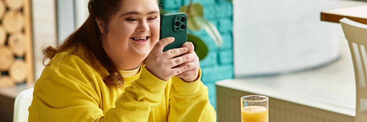 Joven mujer con discapacidad toma un zumo en una cafetería mientras mira el móvil