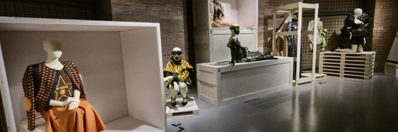 Vista de una sala de exposiciones con maniquíes, diseños de moda y escaleras de acceso