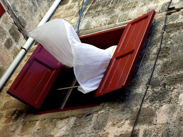 Exterior de una fachada con una ventana abierta y un visillo saliendo por ella por la corriente de aire