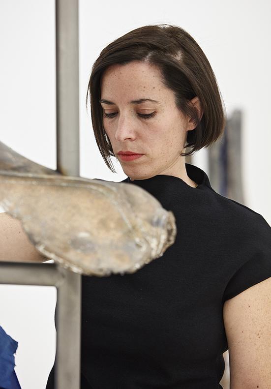 Retrato en color de una mujer joven, morena, con el pelo corto observando una escultura en una exposición