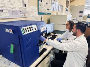Un hombre y en segundo plano una mujer trabajando en una máquina en un laboratorio