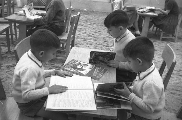 Fotografía de tres niños pequeños leyendo en una mesa en el parque
