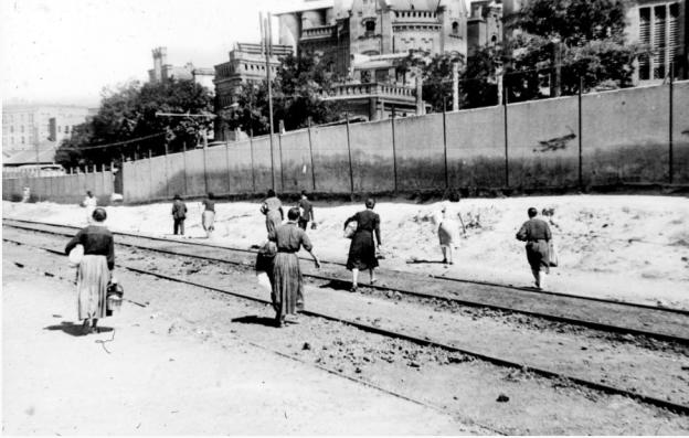 grupo de personas caminando junto a las vías del tren y la fábrica