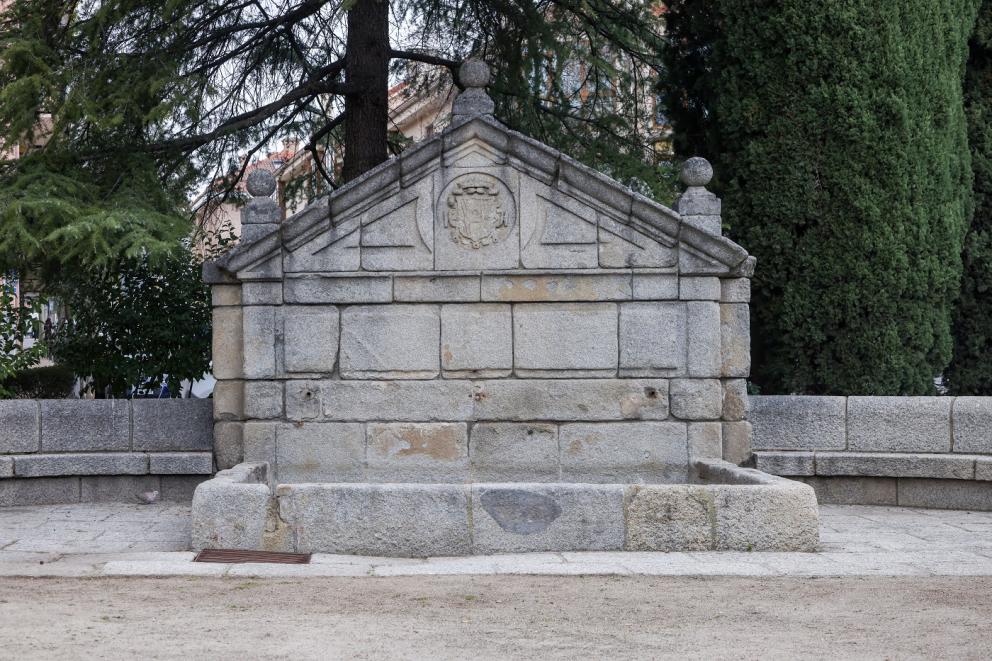 Imagen de una fuente de piedra con frontón triangular y pilón