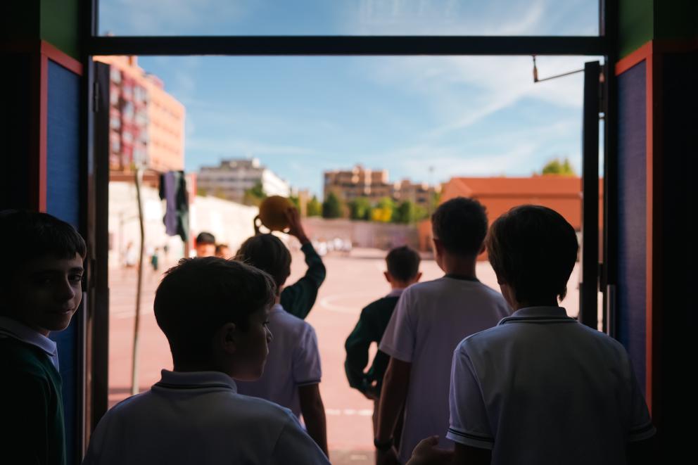 Puerta que sale al patio de un colegio con niños de espaldas sujetando un balón