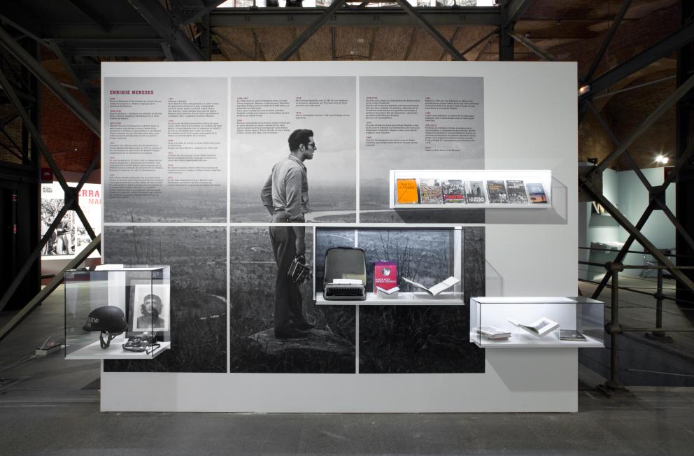 Panel con texto, libros e imagen del fotógrafo Enrique Meneses con su cámara en un paisaje exterior