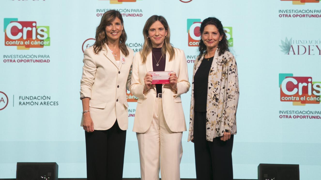 Tres meujeres en el escenario, la del medio recibiendo galardón