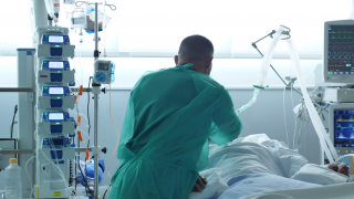 médico con bata verde inclinado de espaldas sobre cama paciente