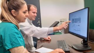 Javier de juan sentado frente a un ordenador señalando la pantalla y al lado de una enfermera
