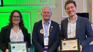 Tres personas dos hombres a la derecha y una mujer a la izquierda con un premio tipo diploma