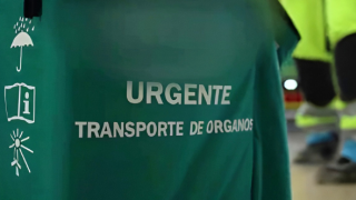 Una nevera con texto llevada por alguien al que se ven las piernas y de fondo una ambulancia