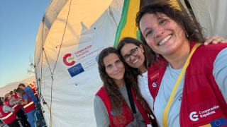 tres mujeres con chalecos rojos posando junto a una tienda de campaña de cooperación