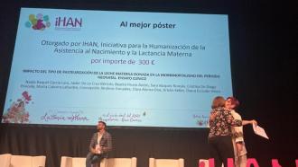 Plano general de dos mujeres que se abrazan en un escenario, una de ellas sostiene un diploma en una mano