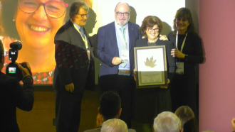 Una mujer con un premio en la mano rodeada de otras tres personas en un escenario