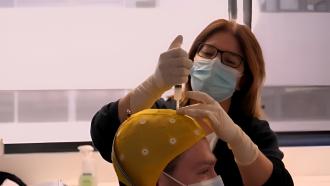 Mujer con ungorro amarillo en la cabeza con agujeritos a través de los cuales una profesional pincha una sustancia