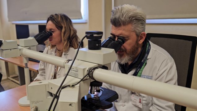 Una mujer y un hombre con batas blancas trabajando en dos microscopios
