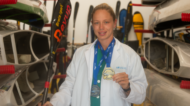 Mujer joven con bata blanca de médica en local con piraguas y posando con una medalla