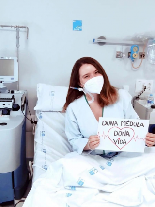 Mujer joven en la cama de un hospital al lado de máquina separadora con cartel Dona médula Dona vida