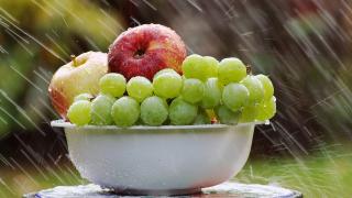 Manzanas, uvas en un frutero con lluvia