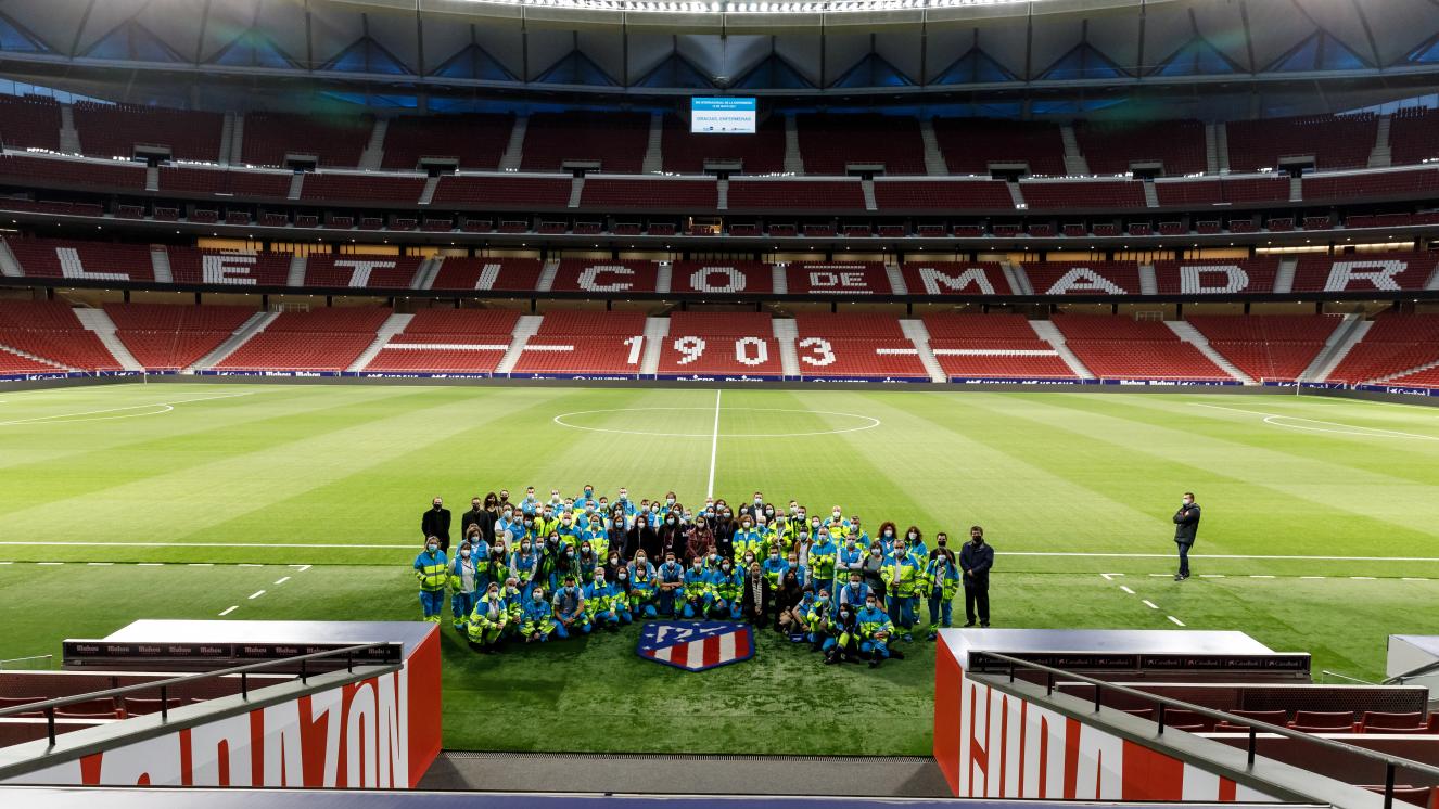 Foto de familia de los profesionales del SUMMA 112 y Hospital Isabel Zendal realizada en el terreno de juego del Wanda Metropolitano, bajo el vídeo marcador con un mensaje de de agradecimiento a las enfermeras.