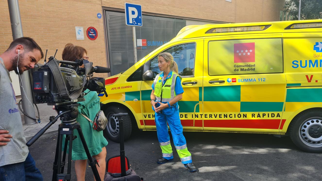 Equipo de operador de cámara junto con su cámara y la redactora realizando una entrevista a una de las Jefas de Guardia del SUMMA 112 para Telemadrid en la calle con le vehículo del SUMMA 112 de fondo