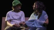Imagen de escena muestra un pareja adolescente de un chico y una chica sentados charlando en un banco