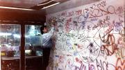 Fotografía de un chico vestido con moda de los 90 firmando una pared llena de grafitis