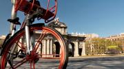 IMAGEN DE LA PUESTA DE ALCALÁ VISTA TRAS LOS RADIO DE LA RUEDA DE UNA BICICLETA ROJA
