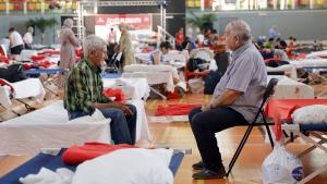 Señores sentados en el pabellón de un polideportivo tras ser evacuados de sus casas