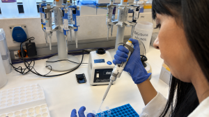 Una mujer investigadora con bata blanca pipeteando el el laboratorio