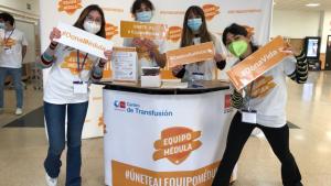 Varios voluntarios detrás de un puesto informativo con logo y lema de equipo médula