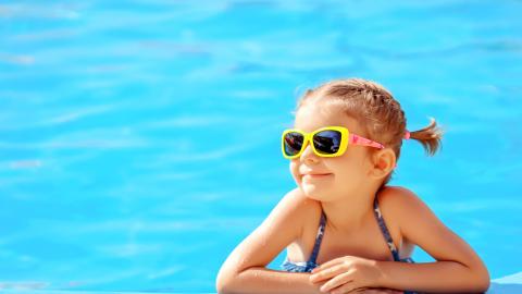 Niña sonriente apoyada en el borde de la piscina
