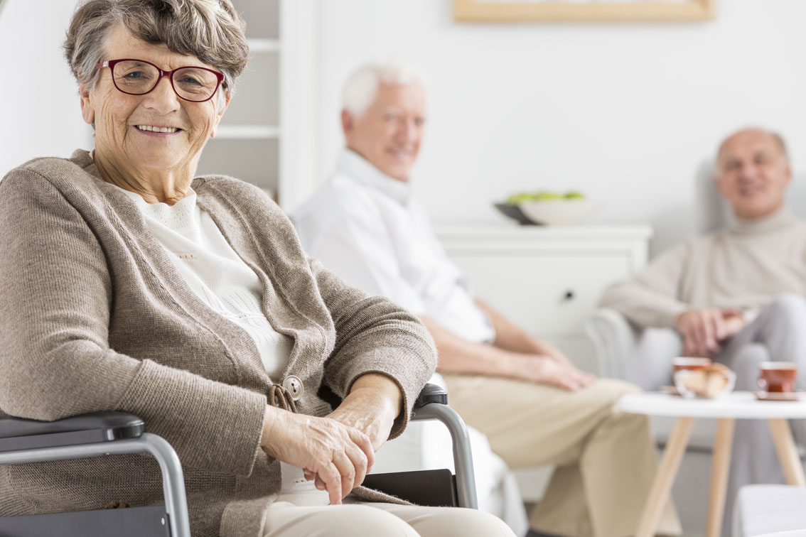 Anciana sentada en primer plano; al fondo, otros ancianos sentados