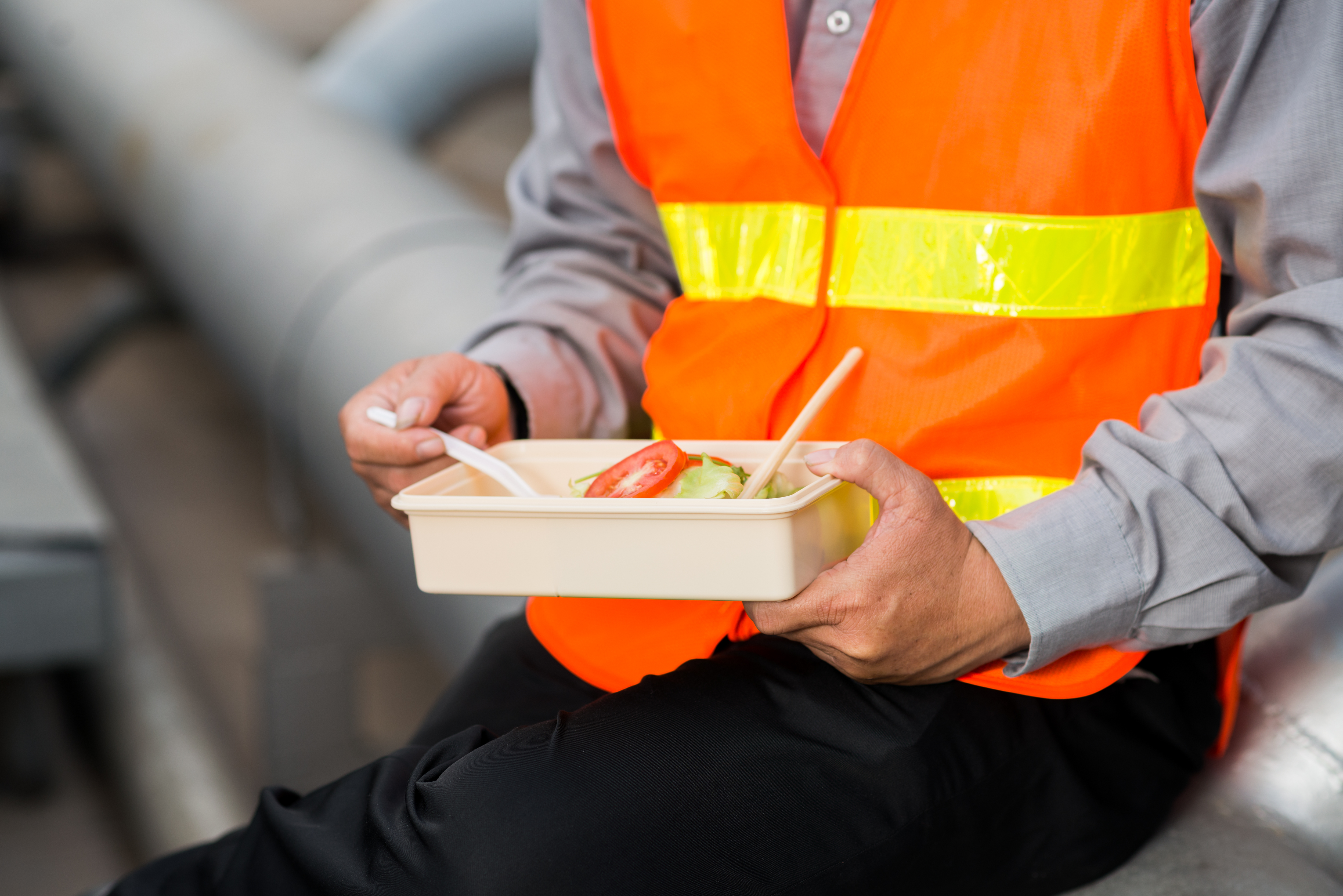 trabajador con chaleco reflectante comiendo de un taper