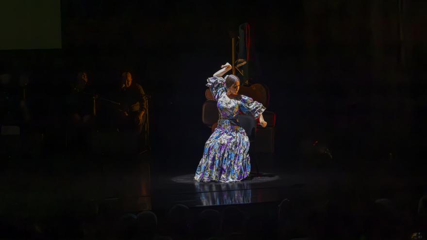 mujer con vestido con volantes baila con los brazos en alto en un escenario