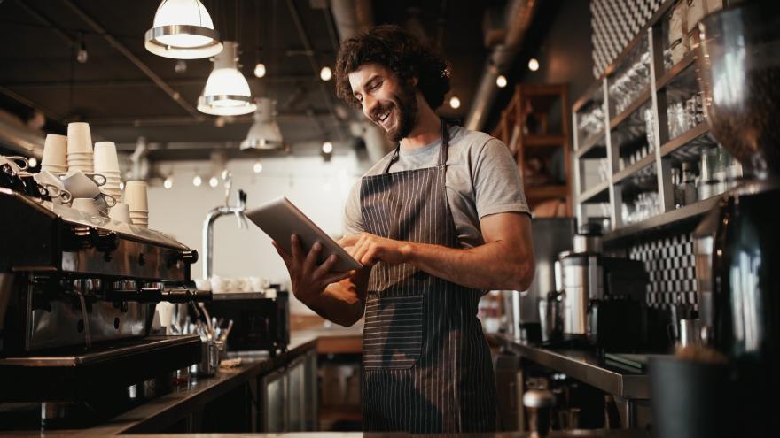 La Comunidad de Madrid reduce el paro un 25,4% el último año, la mayor bajada de la serie histórica en un mes de julio Una chico observa una tablet tras la barra de un café