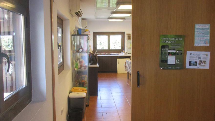 Estancia con puerta madera corredera y al fondo habitación con vitrina y mesa