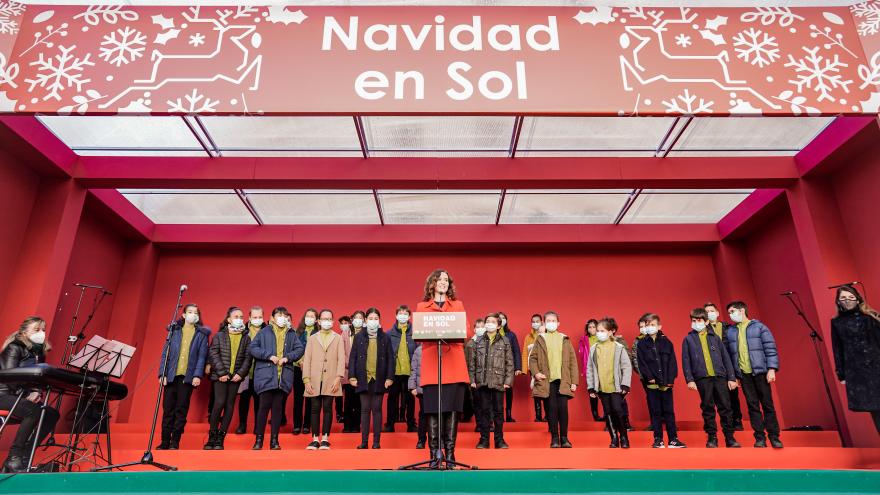 La presidenta interviniendo en el atril con el grupo de niños detrás esperando para cantar