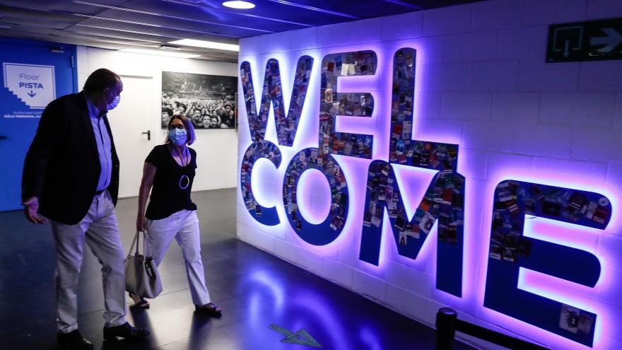 La consejera caminando y hablando con el responsable del Wizink delante de unas letras iluminadas donde pone welcome
