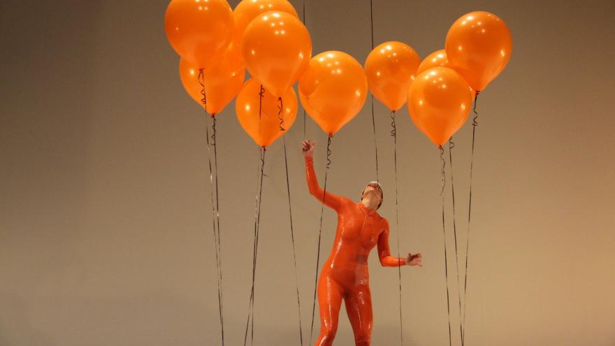 Una mujer vestida de naranja juega con globos del mismo color