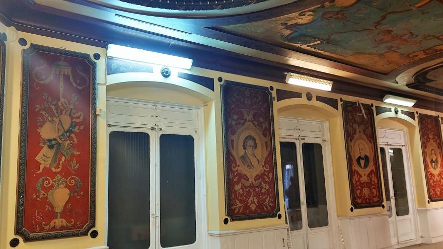 imagen interior del salón con pinturas murales junto a las puertas de los balcones representando a músicos ilustres