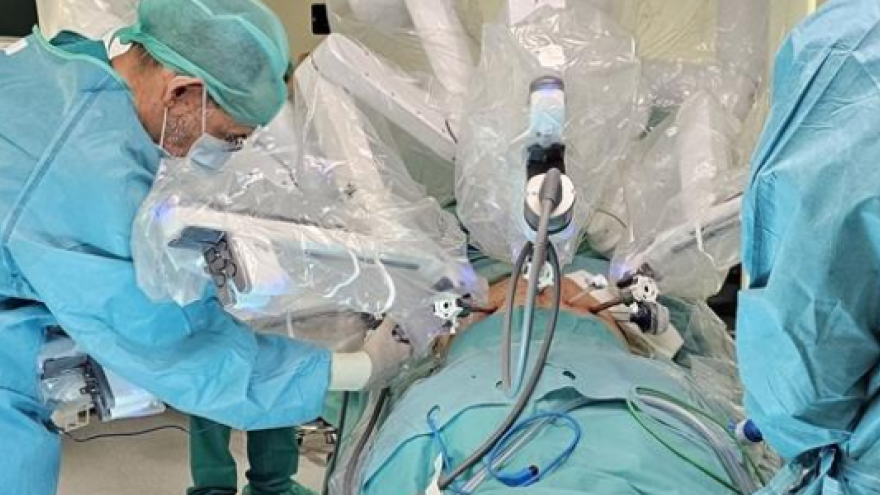 cirujanos en quirófano con un robot con distintos brazos sobre mesa de operaciones