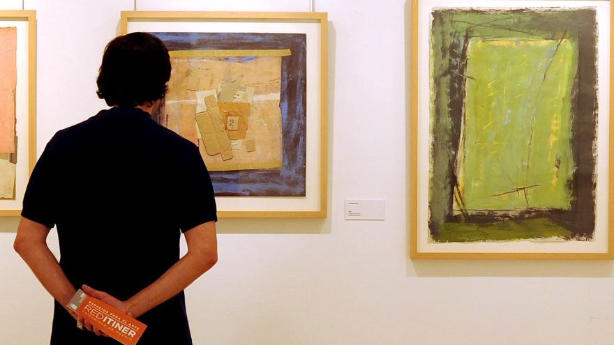 Hombre de pie observando varios cuadros abstractos de colores en la pared de una exposición