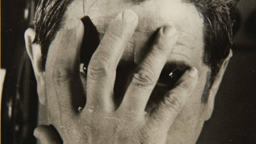 Black and white photo of a man hiding his face with one hand