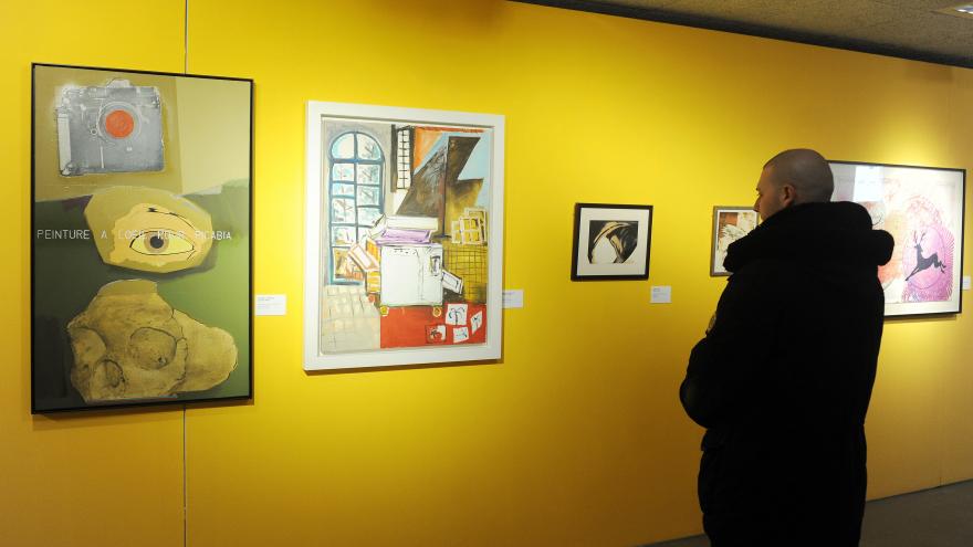 Hombre mirando obras de arte en una exposición con paredes amarillas