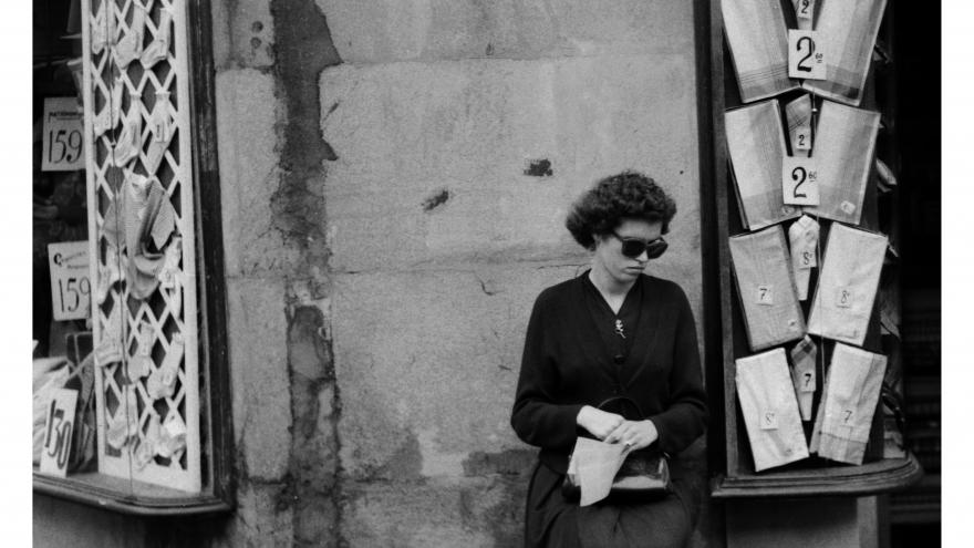 Foto en blanco y negro de una mujer sentada vendiendo cupones en la esquina de una calle de Barcelona