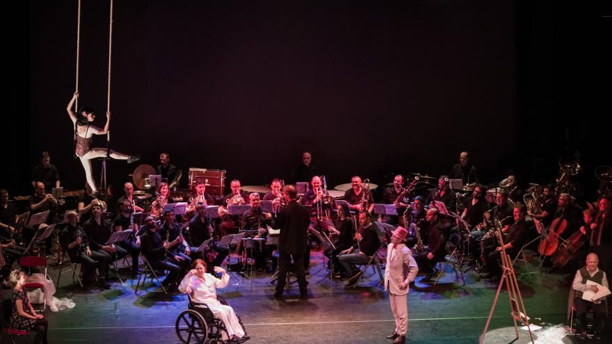 Orquesta sobre un escenario acompañada de varios personajes