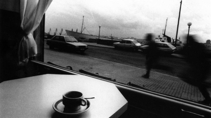 "Un cortao", 1985 © Vari Caramés, VEGAP, Madrid, 2022 Foto en blanco y negro de una persona tomando un café y con una ventana con paisaje de fondo